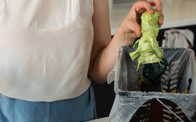 Une femme jette le tron du brocolis dans une poubelle à compost.